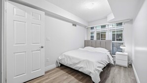 Un dormitorio con cama, mesita de noche, ventana y puerta.