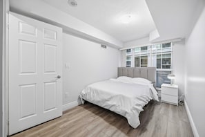 A bedroom with a bed, a nightstand, a window, and a door. - Steps to everywhere! Convenience at its finest! (Toronto)