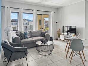 Un salon moderne comprenant un canapé, des fauteuils, une table basse et un coin repas avec un téléviseur.