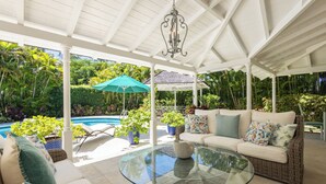 A covered outdoor area with a pool, lounge chairs, a glass table, and a white ceiling structure. - Royal Westmoreland Lonetrees - by Zenbreak (Westmoreland)