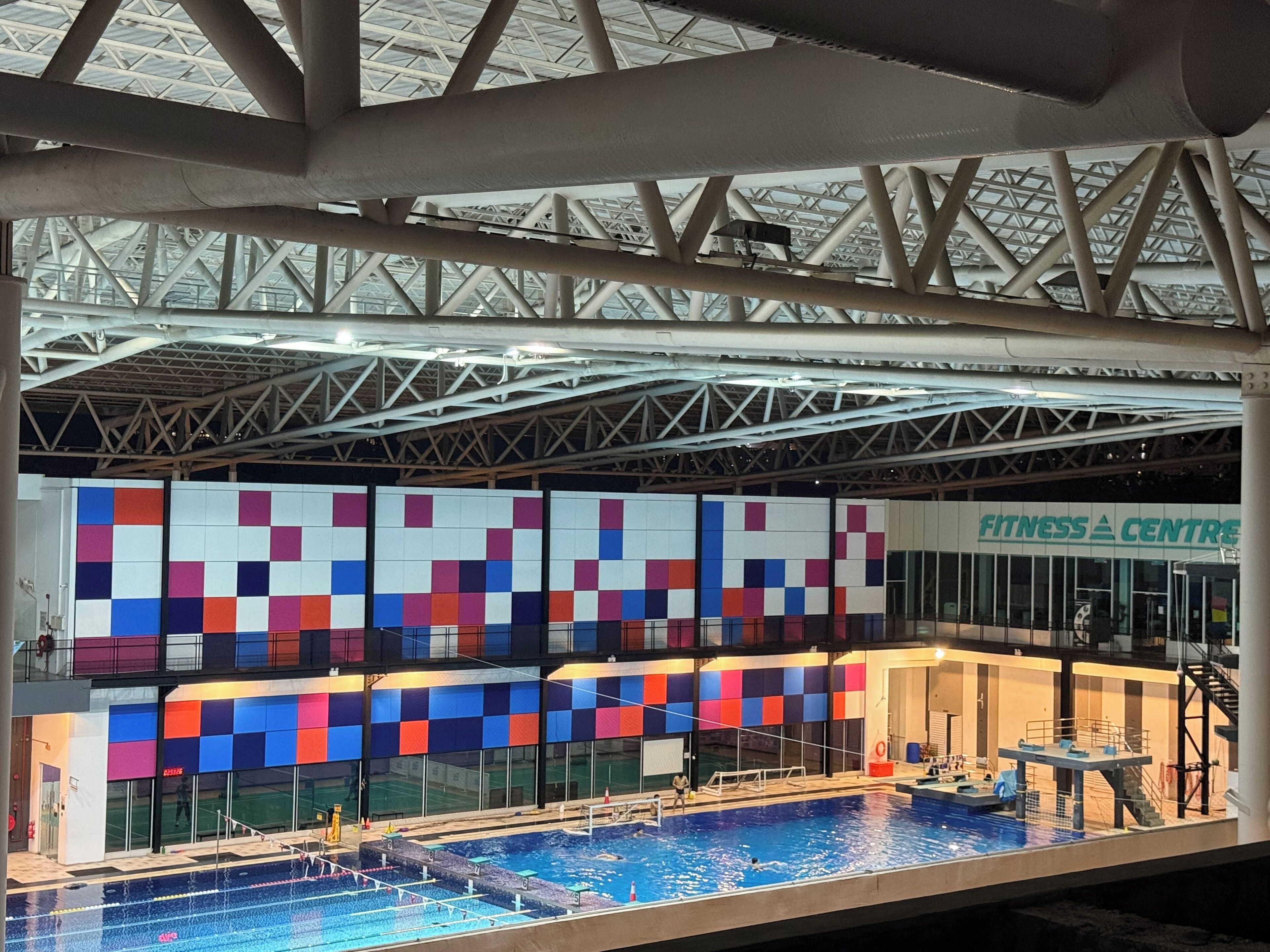 An indoor swimming pool with a diving board, a colorful wall, and a visible 'Fitness Centre' sign.