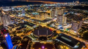 A cityscape at night with illuminated buildings, a prominent tower, and a stadium with a colorful light display. - SPICE Skyview Luxe Tunas 4B3B (Bayan Lepas)