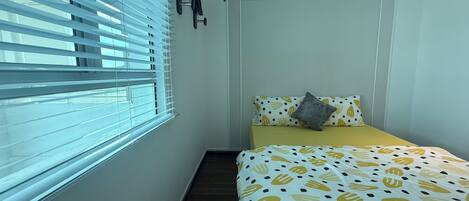A small bedroom with a bed, a window with blinds, and a door.