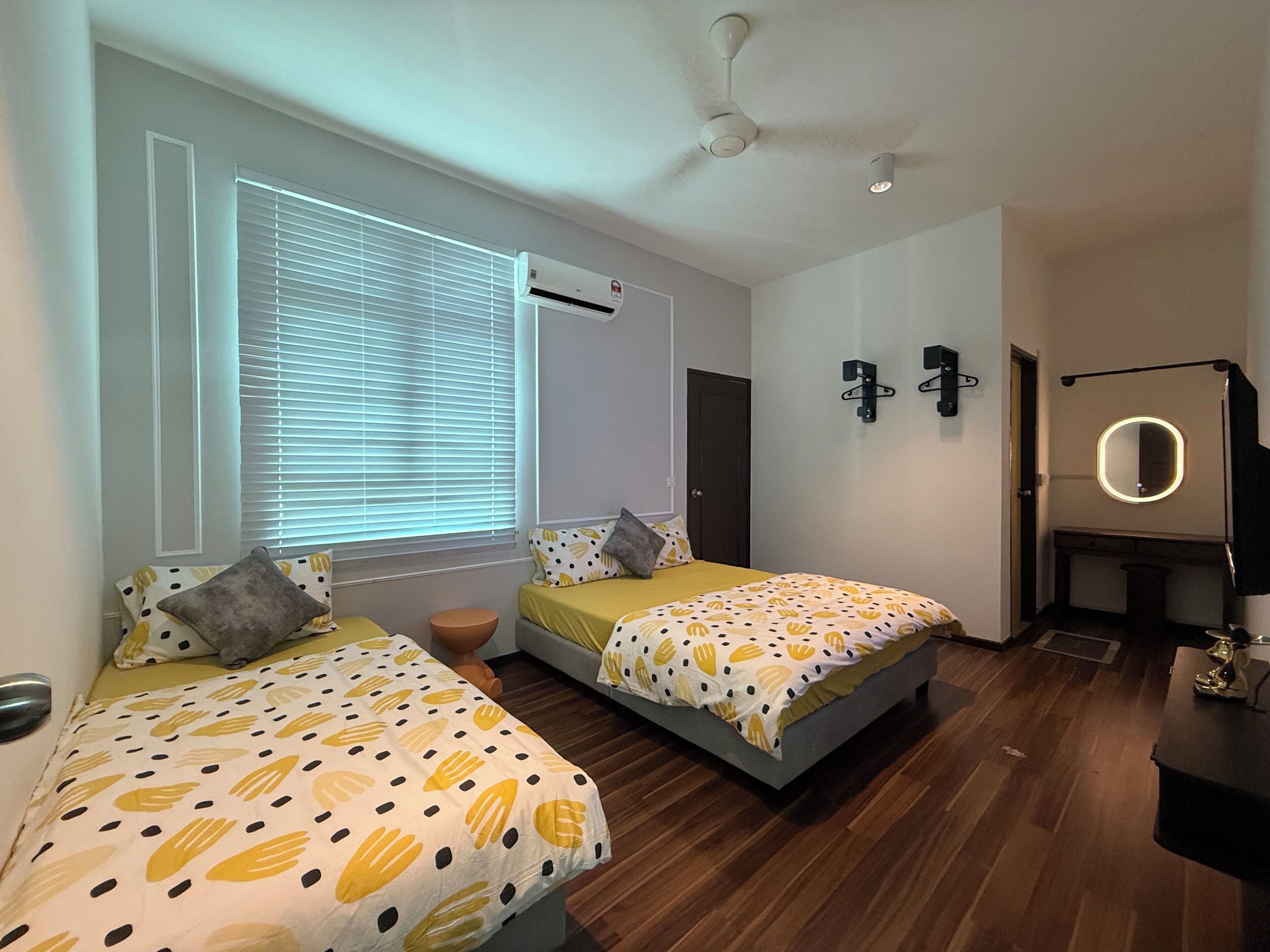 A bedroom with two beds, a ceiling fan, an air conditioning unit, a mirror, and a small desk.