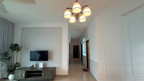 A modern living room with a flat-screen TV, a wooden entertainment unit, a chandelier, and a hallway leading to another room. - SPICE Skyview Luxe Tunas 4B3B (Bayan Lepas)