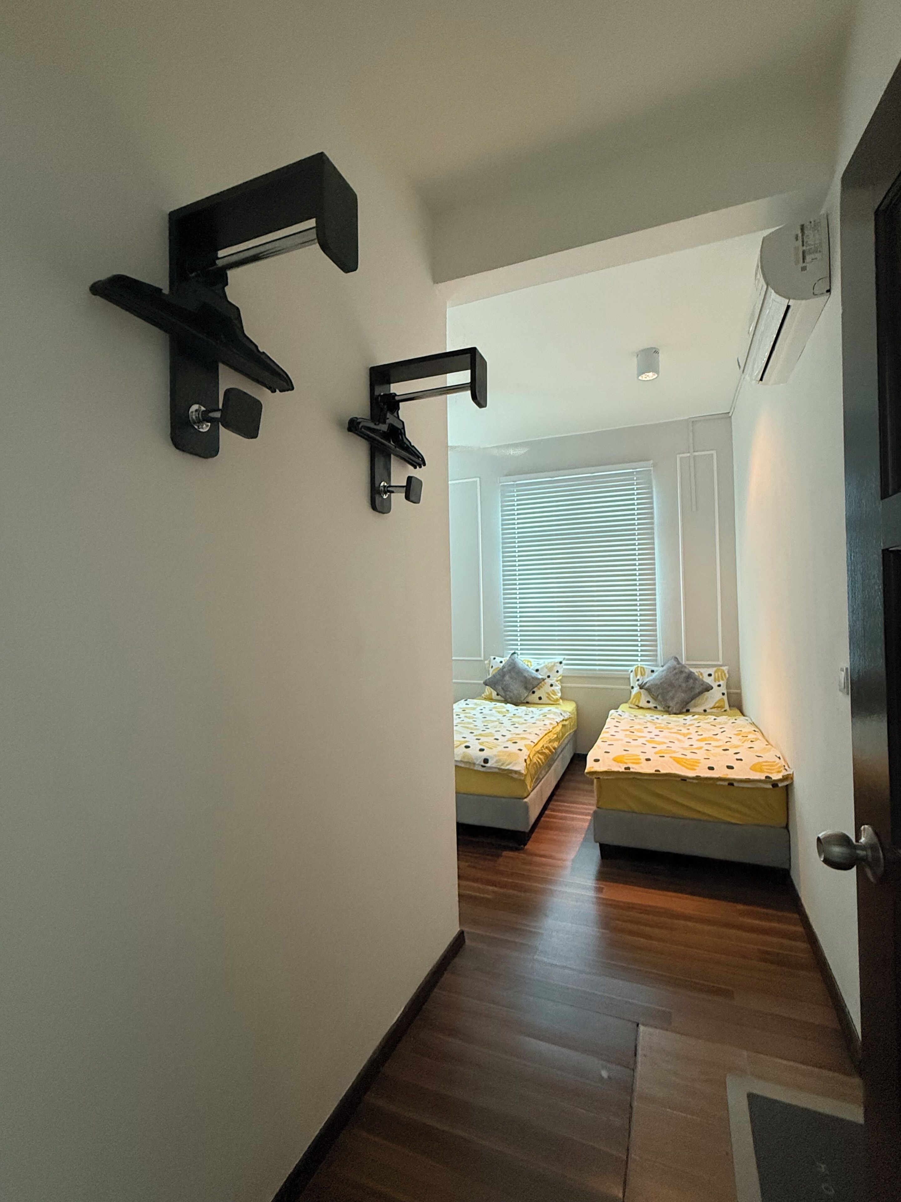 A narrow hallway leading to two bedrooms with wooden flooring, a window with blinds, and a door with a handle.