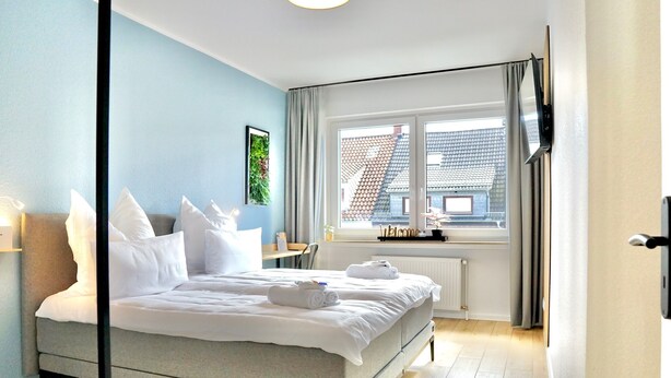 Et moderne hotelværelse med en seng, et vindue med gardiner, en radiator og et fjernsyn ophængt på væggen.