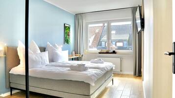 Ein modernes Hotelzimmer mit Bett, einem Fenster mit Vorhängen, einem Heizkörper und einem an der Wand befestigten Fernseher.