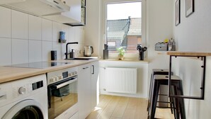 Et kompakt køkken med indbygget ovn, vaskemaskine, et vindue med udsigt og en radiator.