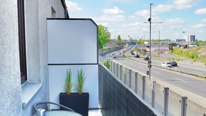 En balkon med et glasbord og stole, en potteplante og udsigt til en motorvej.