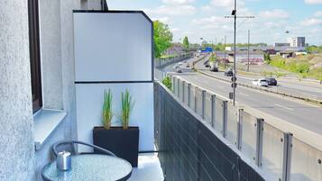 Ein Balkon mit Glastisch und Stühlen, einem Blumentopf und Blick auf eine Autobahn.