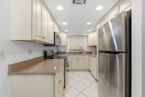 A kitchen with white cabinets, a stainless steel refrigerator, and a granite countertop. - 🏖️ 🏁 Oasis 21: Walk to Beach, Pool + Prime Daytona Event Location! (Daytona Beach Shores)