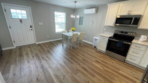 A modern kitchen with a dining area, wooden flooring, white cabinets, and a built-in microwave. - New Build, Modern Studio. Minutes from the Beach. (Navarre)