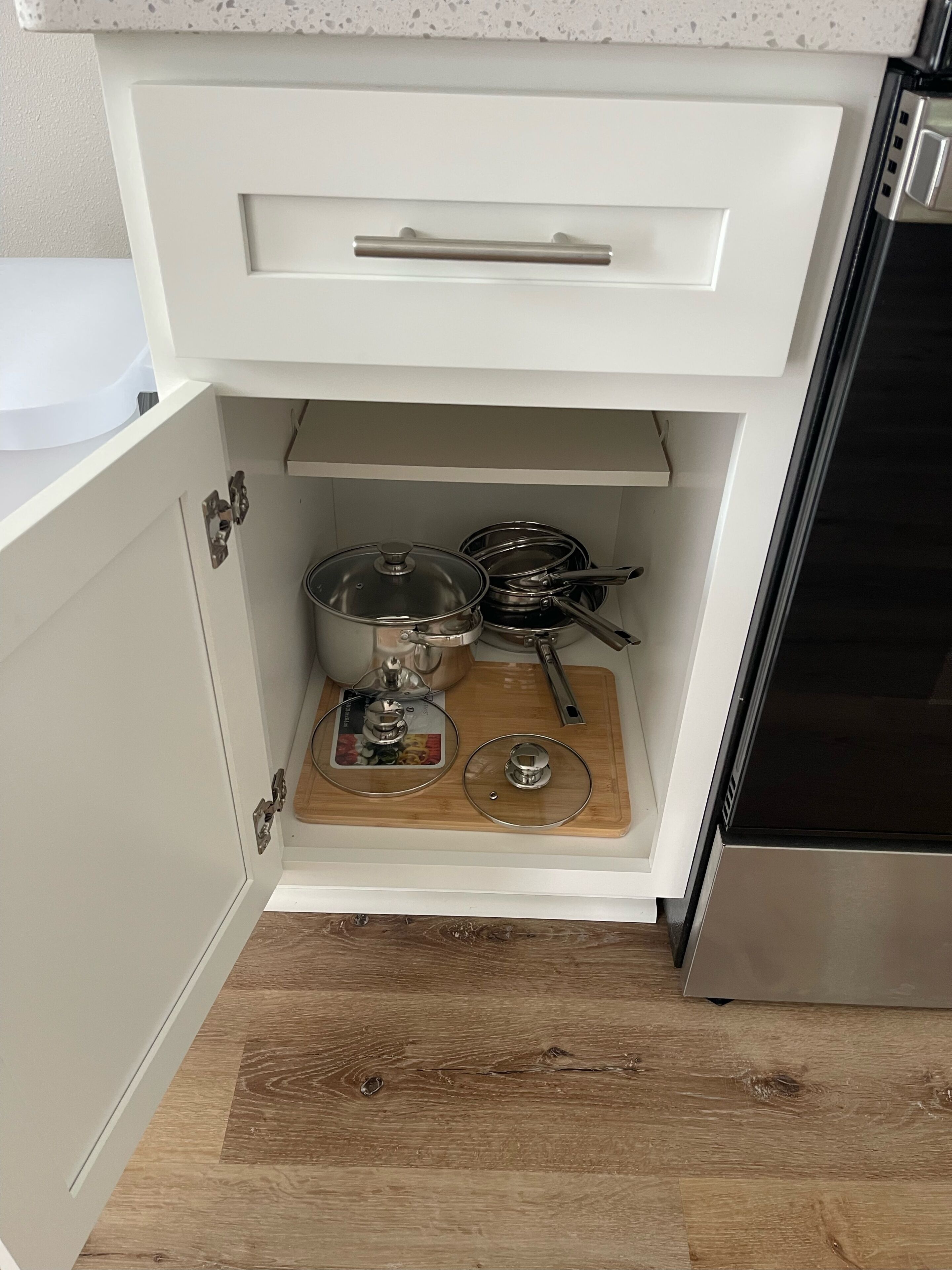 A kitchen with white cabinets, a wooden cutting board, and stainless steel cookware.