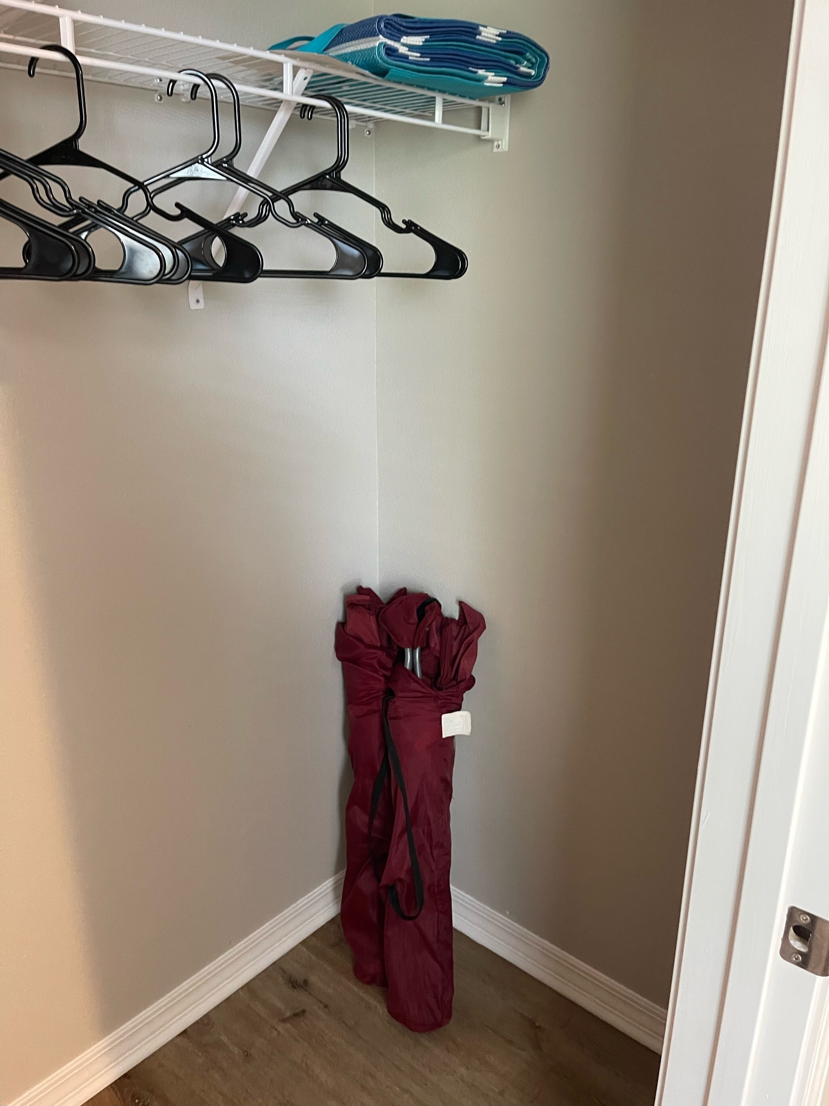 Ein Schrank mit weißer Tür, eine Kleiderstange mit Kleidung und ein gefaltetes Kleidungsstück auf dem obersten Fach.