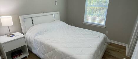 A bedroom with a bed, a nightstand, a ceiling fan, an air conditioner, and a window with blinds.