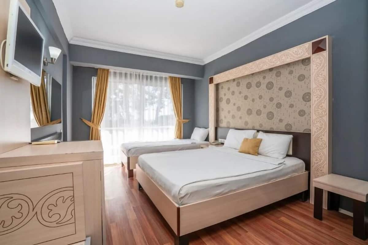 Habitación de hotel con dos camas, televisión, escritorio y un ventanal con cortinas.