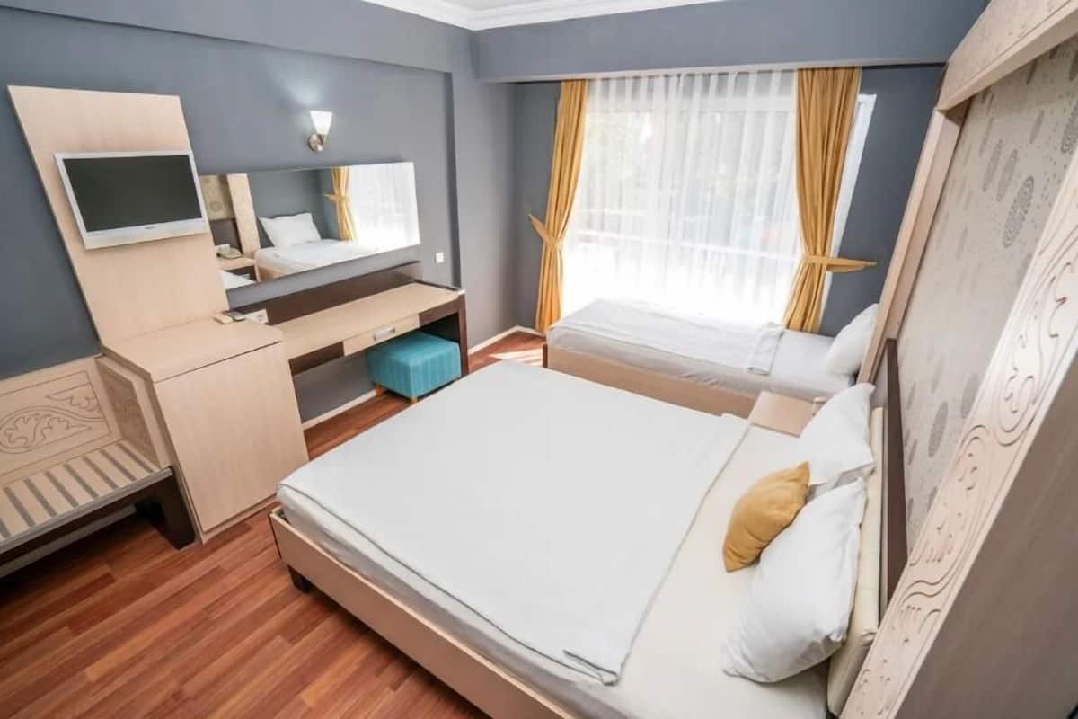 Un dormitorio con cama, escritorio, televisor y ventana con cortinas.