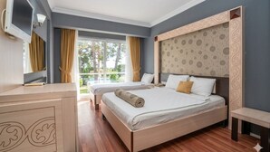 A hotel room with two beds, a TV, a desk, and a large window with curtains. - Club Aperion Beach hotel - All inclusive (Manavgat)