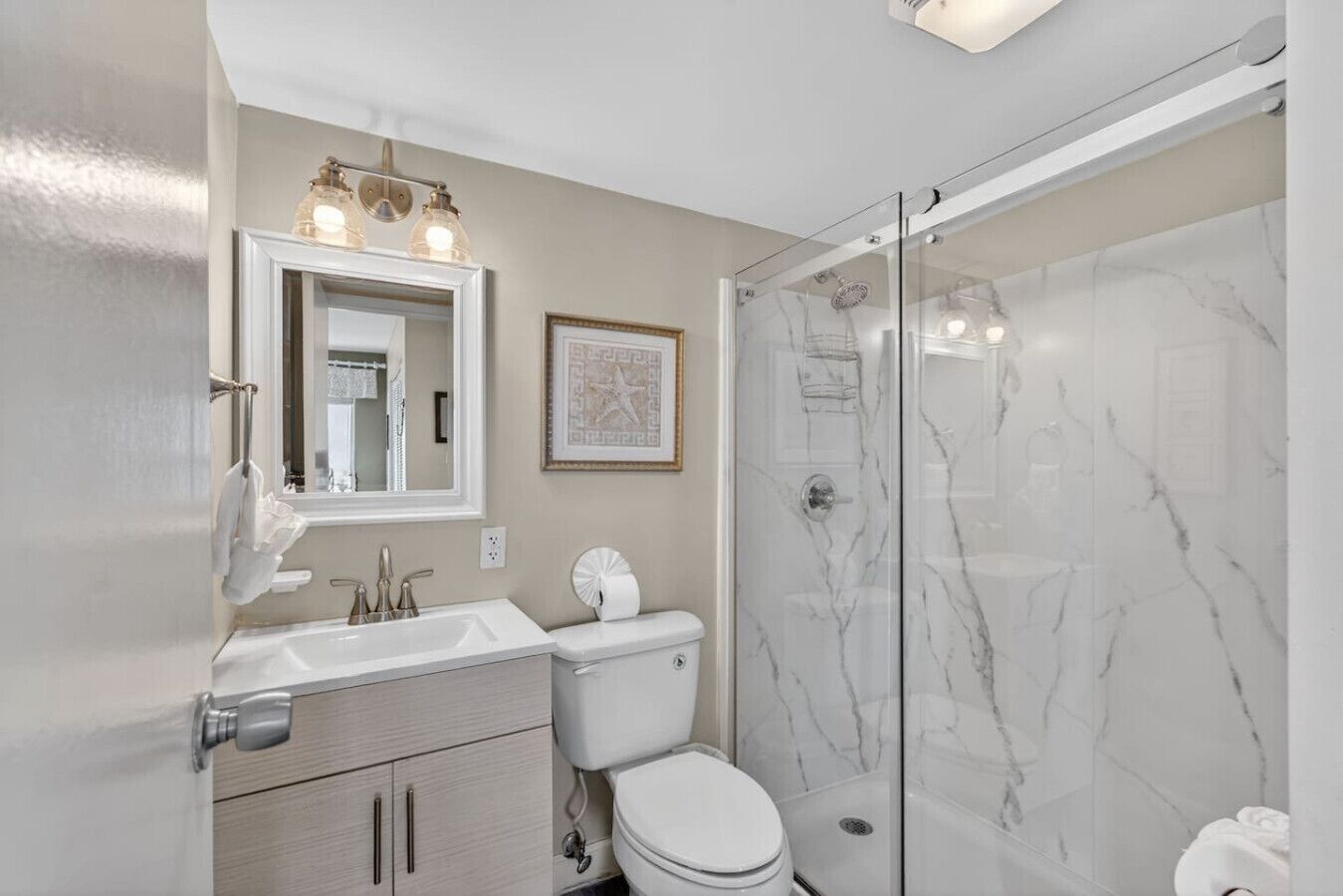 A bathroom with a glass-enclosed shower, a sink with a mirror, and a toilet.