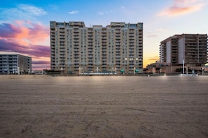 Un immeuble de grande hauteur, doté de nombreux étages, d’un toit plat et d’un sol sablonneux devant l’entrée.