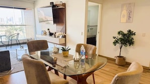 Et moderne spiseområde med et glasbord, polstrede stole, en potteplante og udsigt over bybilledet.