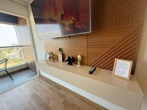 Una habitación de hotel moderna con balcón, televisor de pantalla plana en la pared, pared decorativa de madera y una pequeña mesa con adornos.