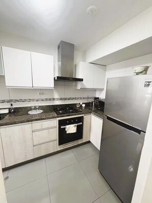 Una cocina con armarios blancos, un refrigerador de acero inoxidable, una estufa a gas y un horno empotrado.