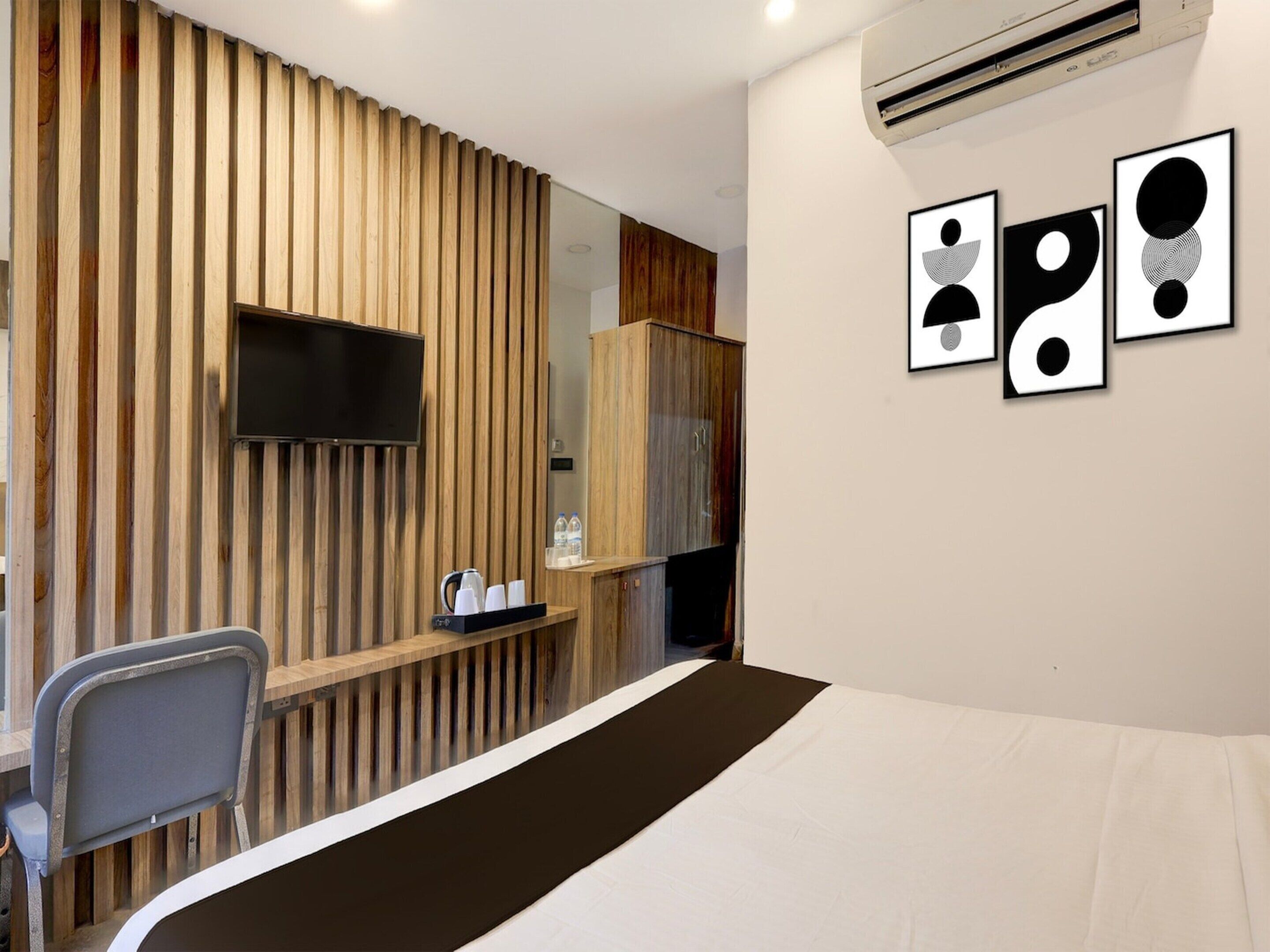 A hotel room with a bed, a TV mounted on the wall, a desk with a chair, and a shelf with toiletries.