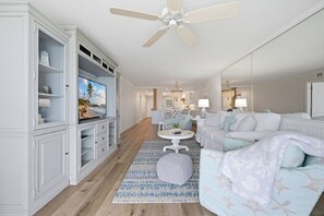A spacious living room with a television, white furniture, a ceiling fan, and a view into the kitchen. - Luxury Waterfront Escape Near St. Pete Beach & Pass-a-Grille | Isla Del Sol Paradise (Isla Del Sol)