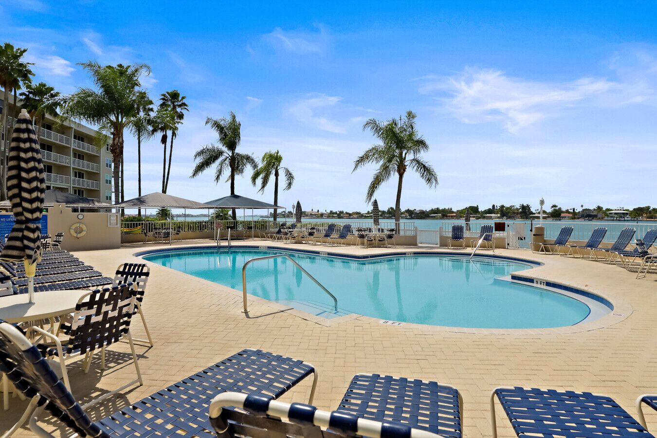 A pool area with lounge chairs, palm trees, and a clear view of the ocean.