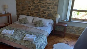 A bedroom with a bed, a nightstand, a wooden table, and a stone wall. - Bed and breakfast with swimming pool (Trausse)