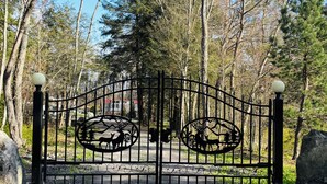 Een toegangspoort met decoratieve metalen versiering, omgeven door bomen en een grindpad.