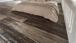 Een slaapkamer met houten vloer, een bed met beige beddengoed en een wit plafond.