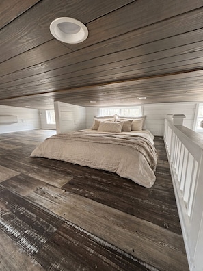 Ein Schlafzimmer mit Holzboden, einem Bett mit beige farbenem Bettzeug und einer weißen Decke.