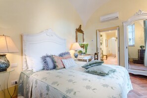 A bedroom with a bed, a nightstand, a lamp, a mirror, and a door leading to another room. - Apartment in Lucca With Private Garden (Lucca)