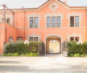 A two-story building with a symmetrical facade, a central entrance with an arch, and a car parked in the driveway. - Apartment in Lucca With Private Garden (Lucca)