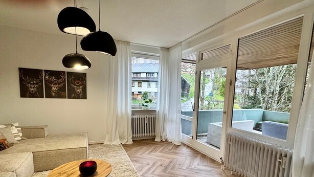 Una sala de estar moderna con un sofá, una mesa de centro y vistas a un balcón con mobiliario exterior.