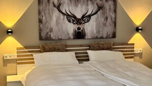 Un dormitorio con cama, cabecera, mesitas de noche, luces fijadas a la pared y un cuadro grande de un ciervo.