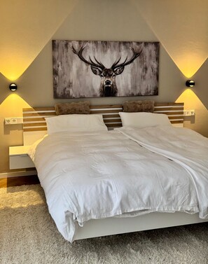 Ein Schlafzimmer mit einem Bett, einem Kopfteil, Nachttischen, Wandleuchten und einem großen Bild eines Rehs.