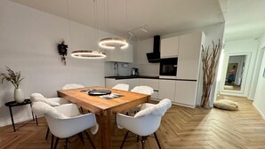 Una cocina moderna con armarios blancos, una mesa de comedor de madera con sillas, luces colgantes y una estufa negra.