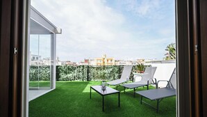 Un balcón con césped artificial, dos sillones de descanso y una mesa con un objeto de vidrio.