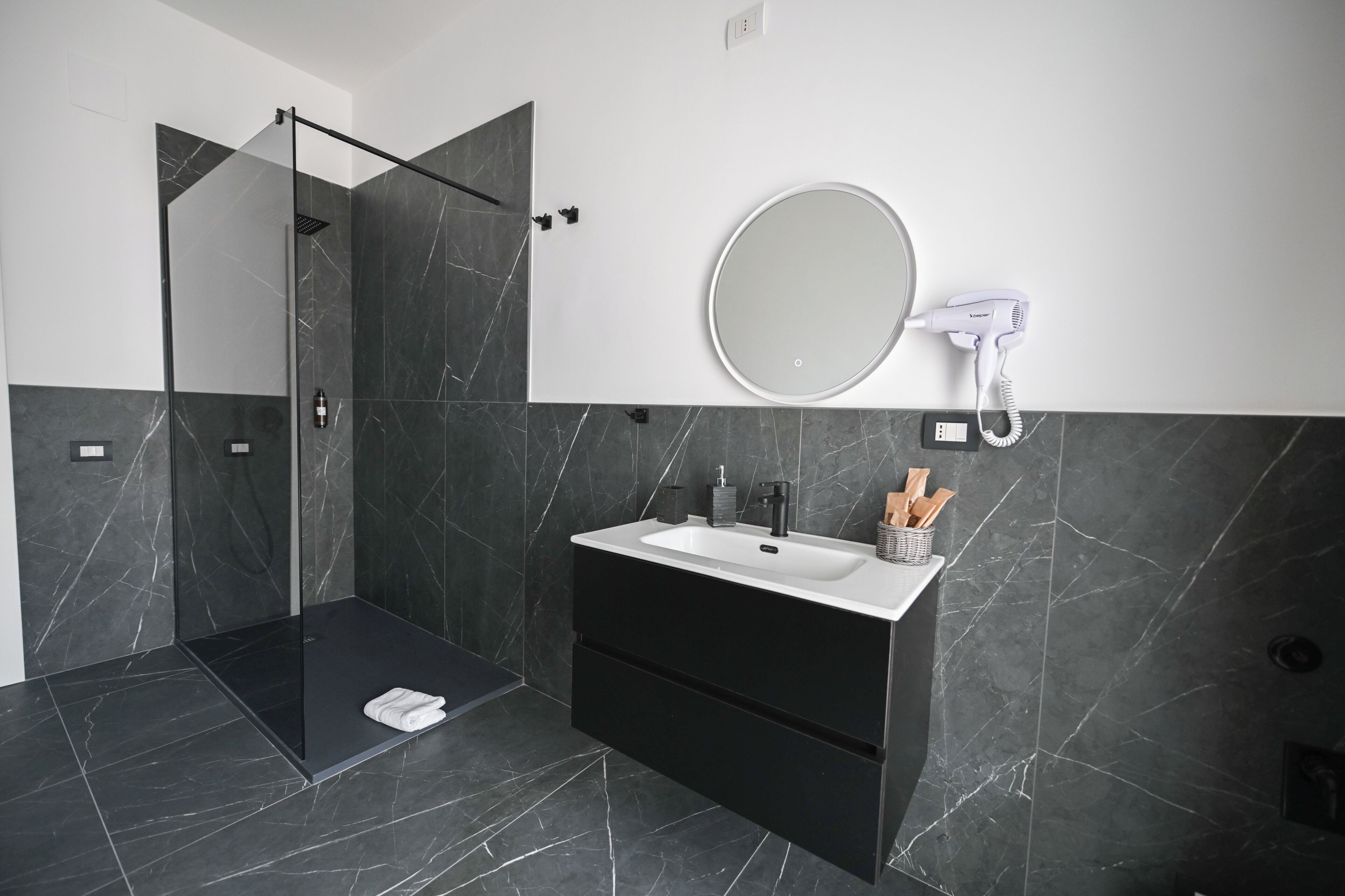 Une salle de bain moderne avec une douche à parois de verre, un meuble-lavabo et un sèche-cheveux fixé au mur.