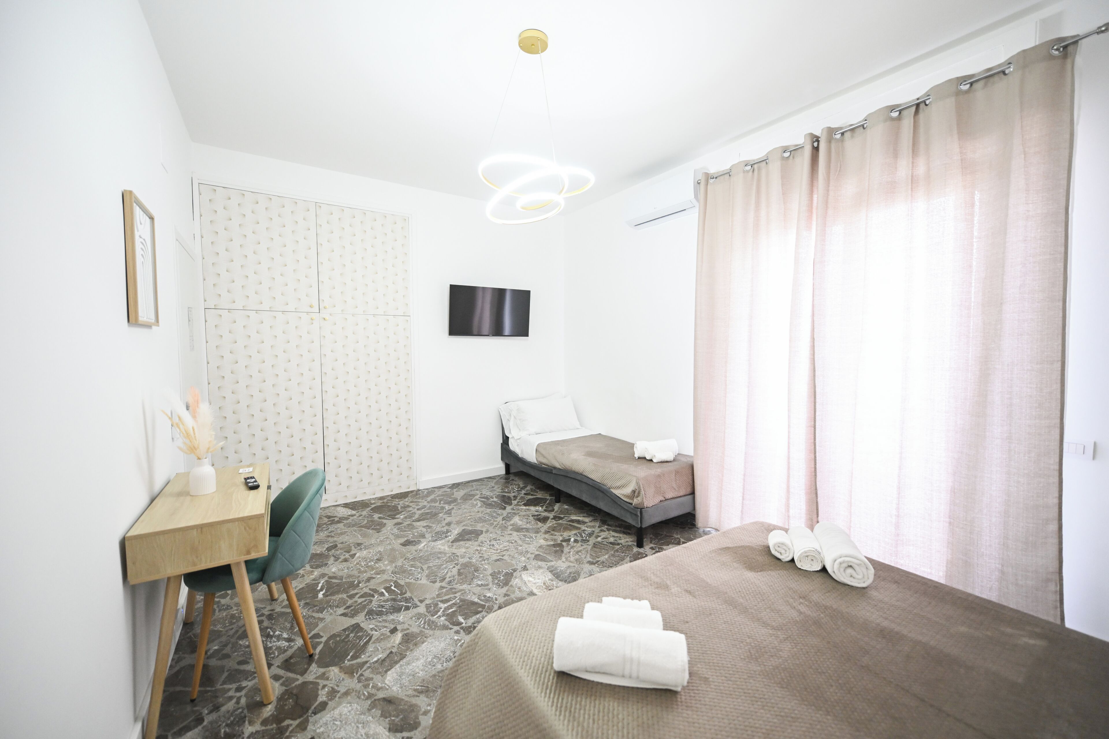 Ein Schlafzimmer mit Bett, Schreibtisch, Stuhl, Fernseher und Vorhängen.