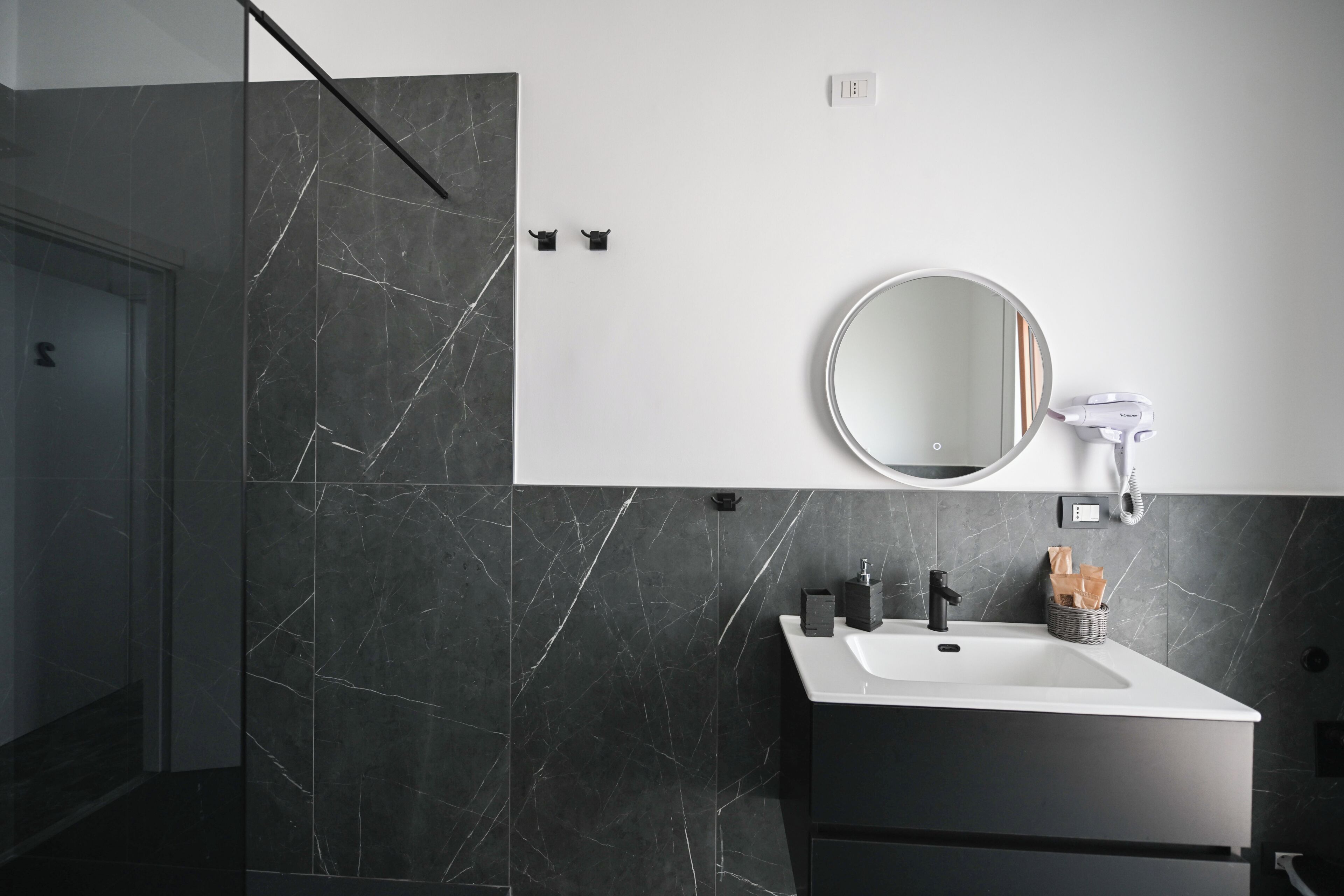 Un baño moderno con diseño de mármol blanco y negro, un espejo redondo, un lavabo blanco y un mueble negro.