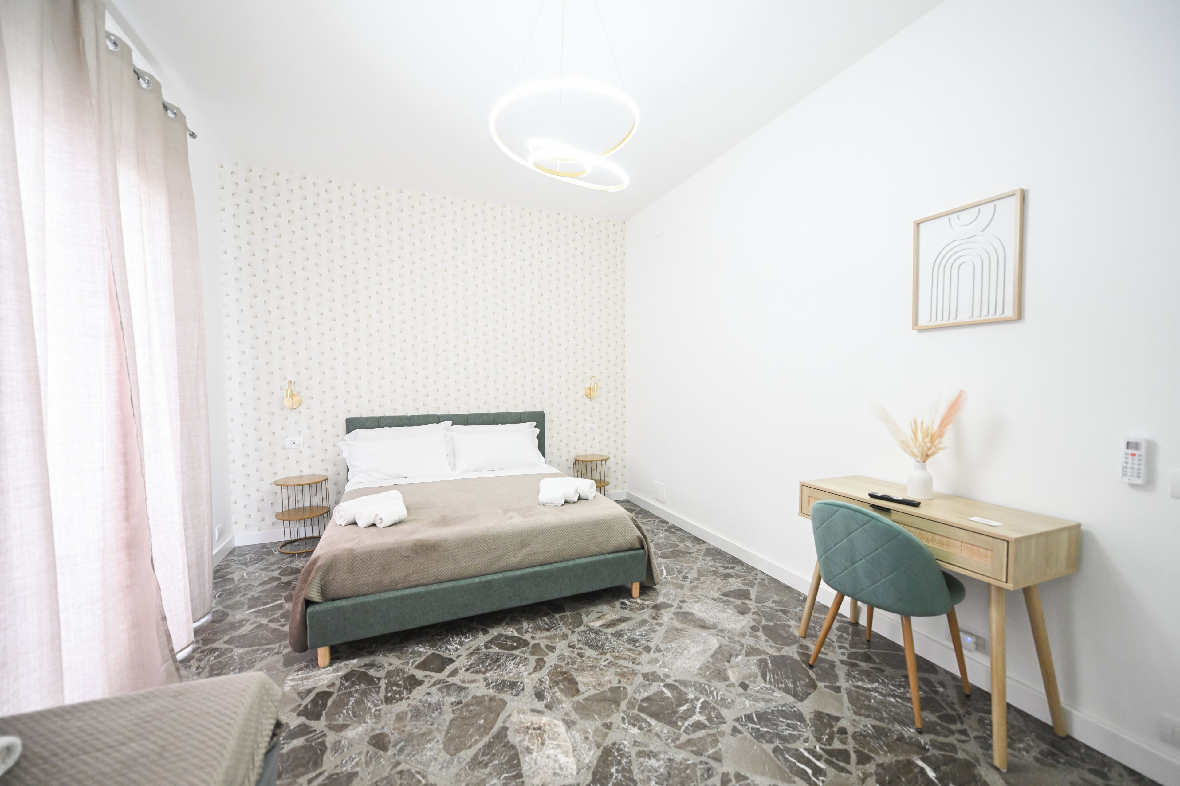 A bedroom with a bed, a desk, a chair, a wall-mounted artwork, and a patterned wall.