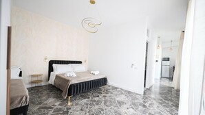 Un dormitorio moderno con una cama, una mesita de noche, una lámpara de pared y una zona de cocina al fondo.