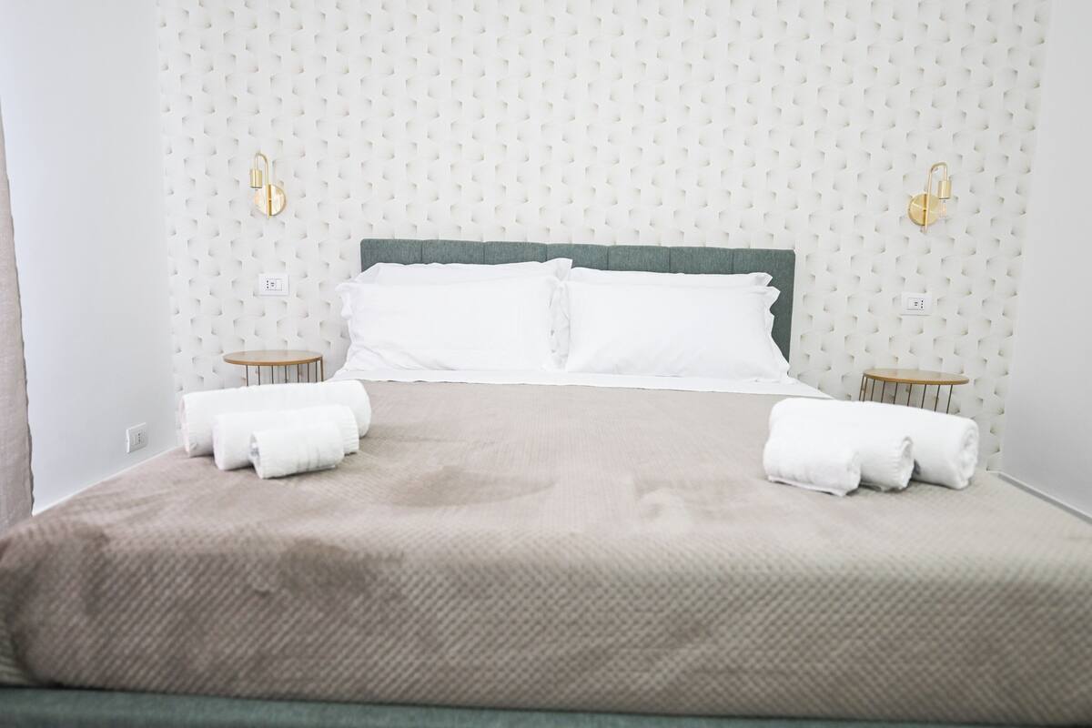 A neatly made bed with white linens, two bedside tables, and a wall with a textured pattern.