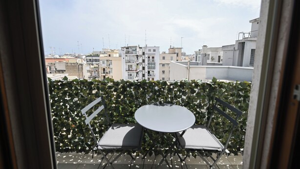 Un balcón con mesa y sillas, un seto y vistas a edificios.