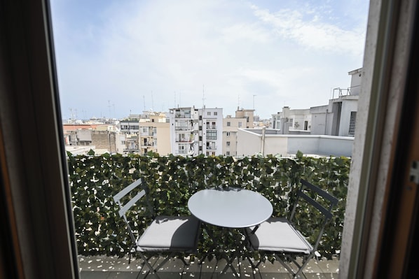 Ein Balkon mit Tisch und Stühlen, einer Hecke und Blick auf Gebäude.
